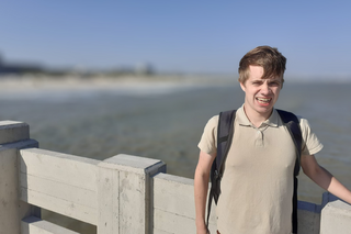 Buitenhof Reizen voor mensen met een verstandelijke beperking - Ondernemend - Belgische Kust - reiziger met wapperende haren op een brug met zeezicht Buitenhof Reizen voor mensen met een verstandelijke beperking - Ondernemend - Belgische Kust - reiziger met wapperende haren op een brug met zeezicht