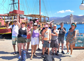 Buitenhof Reizen voor mensen met een verstandelijke beperking - Ondernemend - Grieks genieten op Kreta - reizigers met armen in de lucht voor de boot Buitenhof Reizen voor mensen met een verstandelijke beperking - Ondernemend - Grieks genieten op Kreta - reizigers met armen in de lucht voor de boot