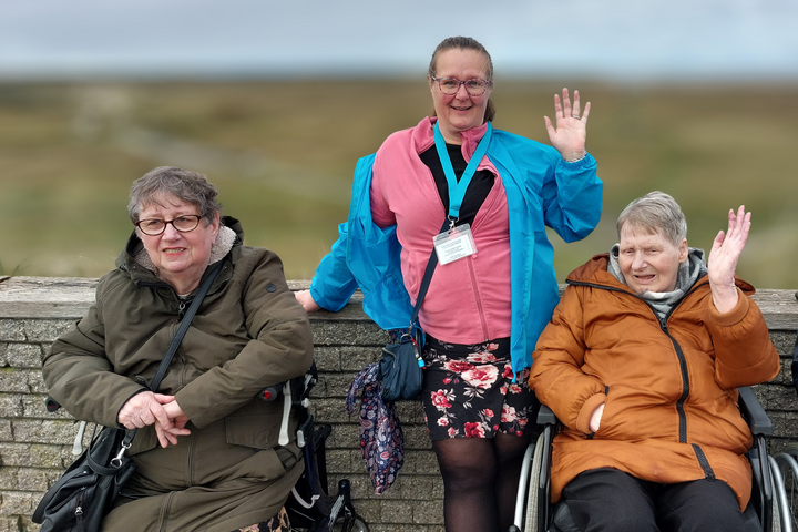 Buitenhof Reizen voor mensen met een verstandelijke beperking - Zorg - Zeehonden spotten op Texel - Begeleider met twee zwaaiende reizigers Buitenhof Reizen voor mensen met een verstandelijke beperking - Zorg - Zeehonden spotten op Texel - Begeleider met twee zwaaiende reizigers