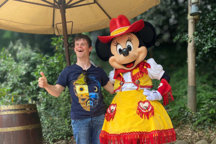 Buitenhof Reizen voor mensen met een verstandelijke beperking - Jongeren - Magisch Disneyland - Reiziger met mini mouse en duim in de lucht Buitenhof Reizen voor mensen met een verstandelijke beperking - Jongeren - Magisch Disneyland - Reiziger met mini mouse en duim in de lucht