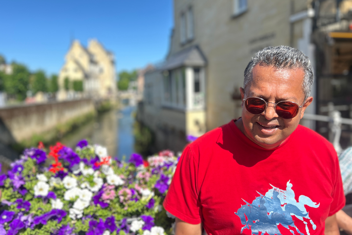 Buitenhof Reizen - Ondernemend- Valkenburg Cauburg - begeleide groepsreizen voor mensen met een verstandelijke beperking - reiziger op een bruggetje in Valkenburg met de bloemen en gebouwen op de achtergrond Buitenhof Reizen - Ondernemend- Valkenburg Cauburg - begeleide groepsreizen voor mensen met een verstandelijke beperking - reiziger op een bruggetje in Valkenburg met de bloemen en gebouwen op de achtergrond